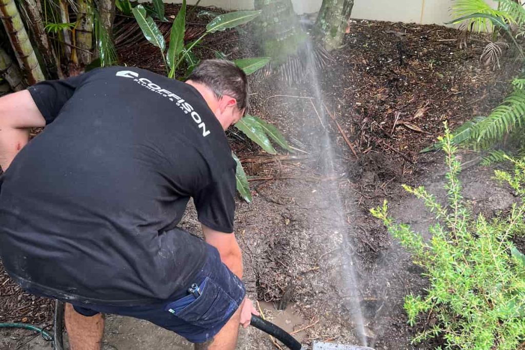Coffison Plumbing team member locating and exposing a burst pipe for repair in a residential garden.