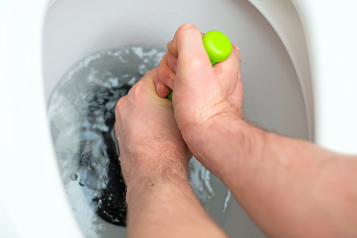 Plumber using a plunger to clear a blocked toilet during a repair in a residential bathroom.