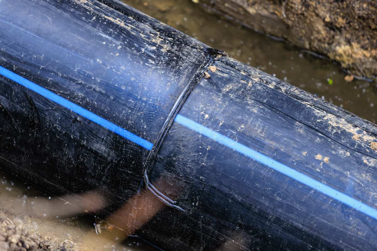 Close-up of a cracked and leaking PVC pipe in need of repair or relining.
