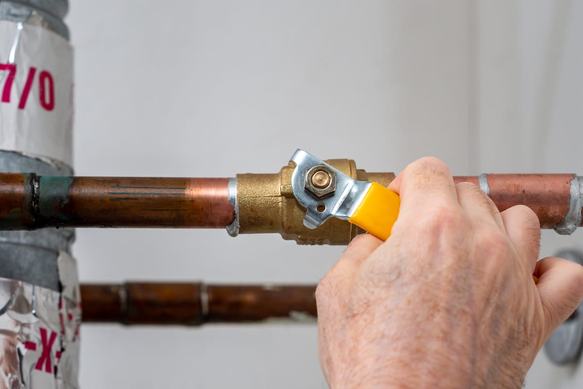 Hand turning off a valve on a copper gas pipe in a Brisbane property to isolate a suspected burst.