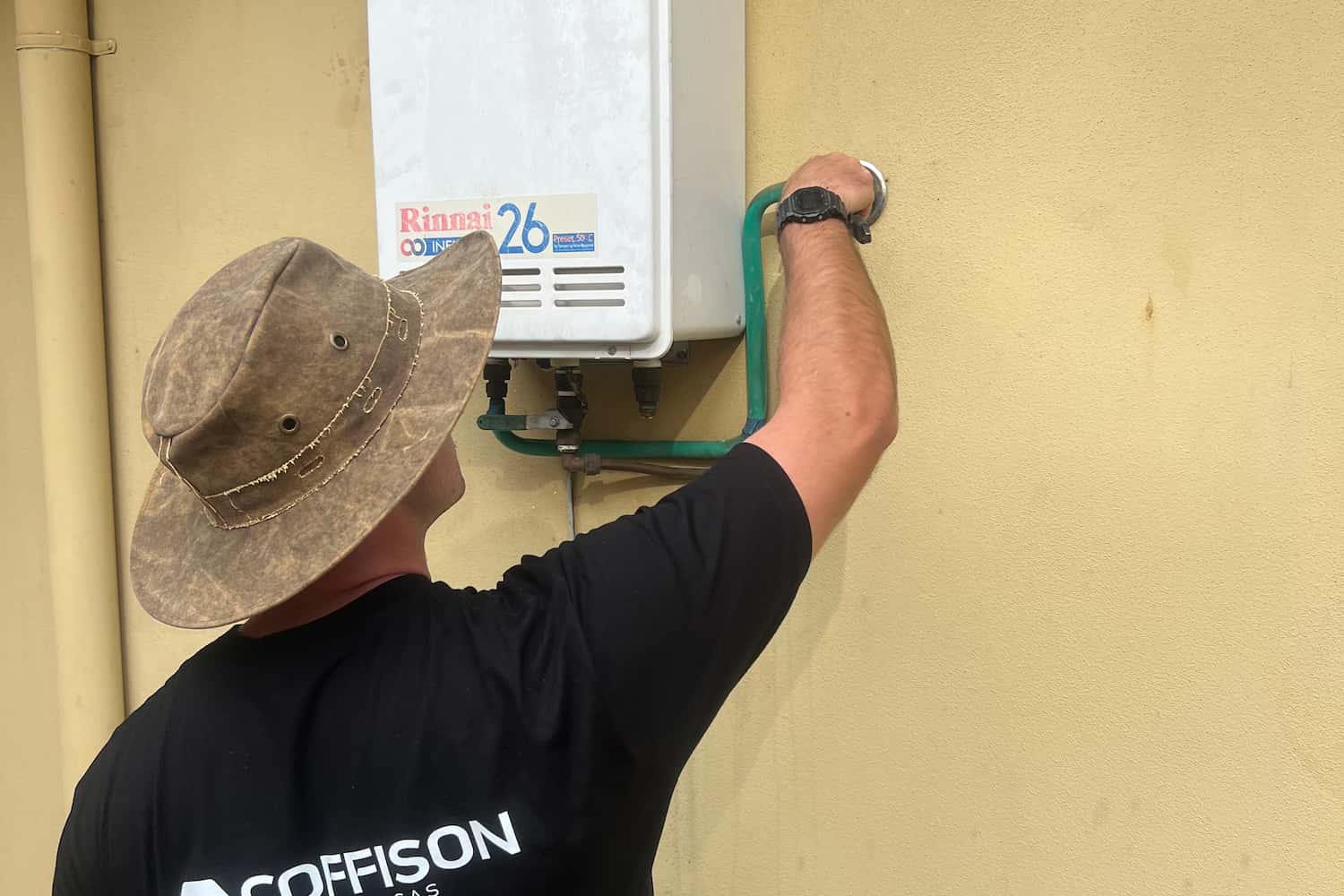 Coffison Plumbing technician inspecting an outdoor Rinnai hot water system unit on a residential property.