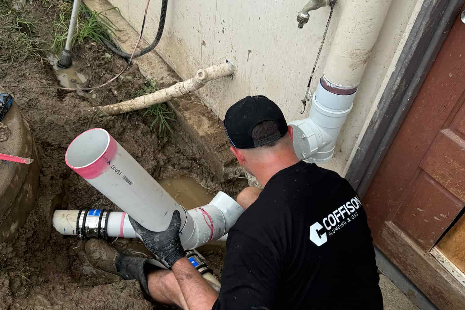 Coffison Plumbing technician repairing and replacing external PVC drainage pipes at a residential property.