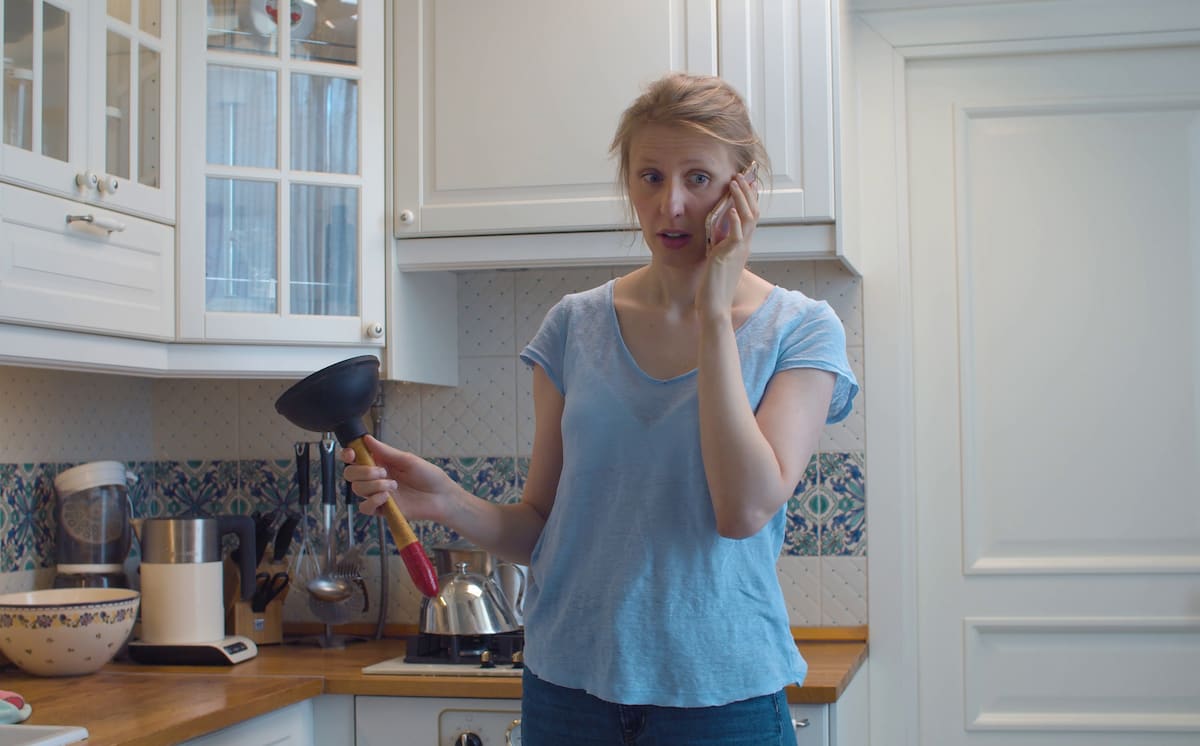 Confused tenant on the phone holding a plunger, unsure about responsibility for a blocked drain.