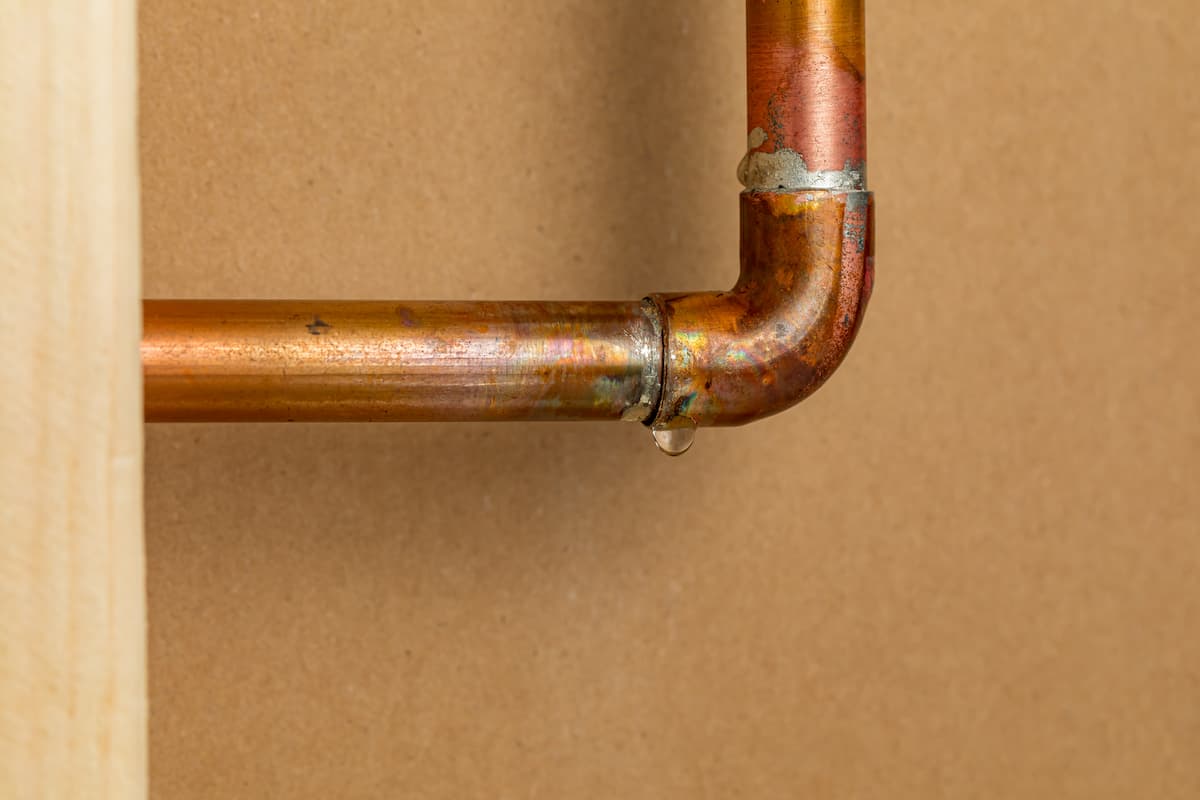 Close-up of a leaking copper pipe with water droplet at joint.