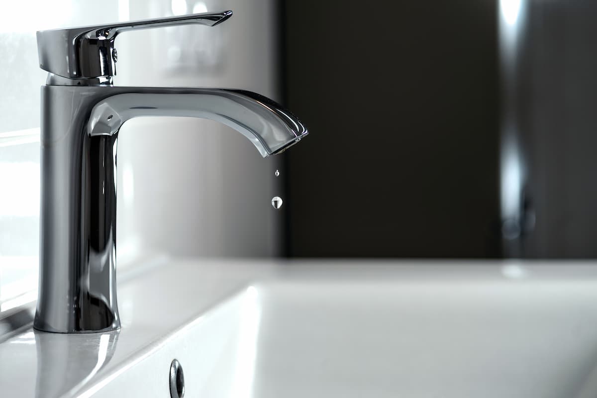 Close-up of a dripping tap with water drop hanging from spout in a home bathroom.