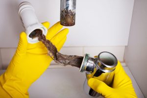 Gloved hands removing hair blockage from a bathroom drain trap.