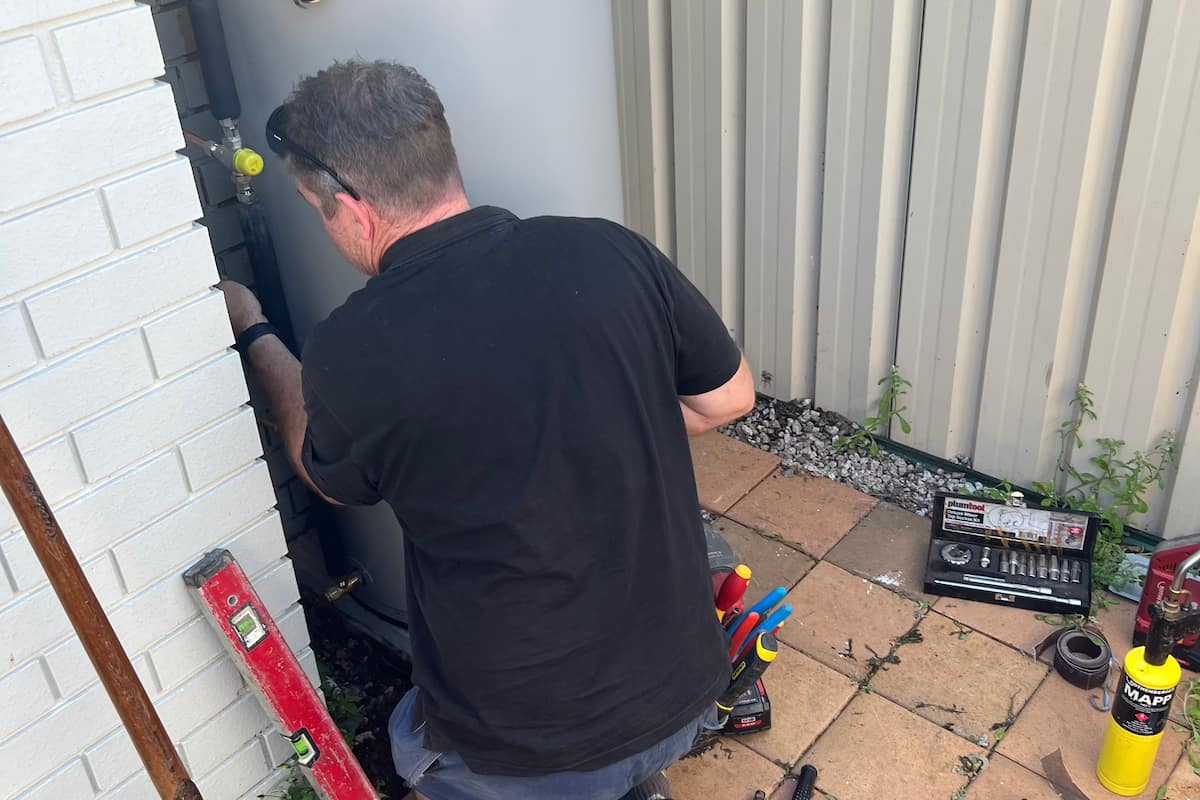 Coffison Plumbing technician replacing a residential hot water system with tools and fittings on site.
