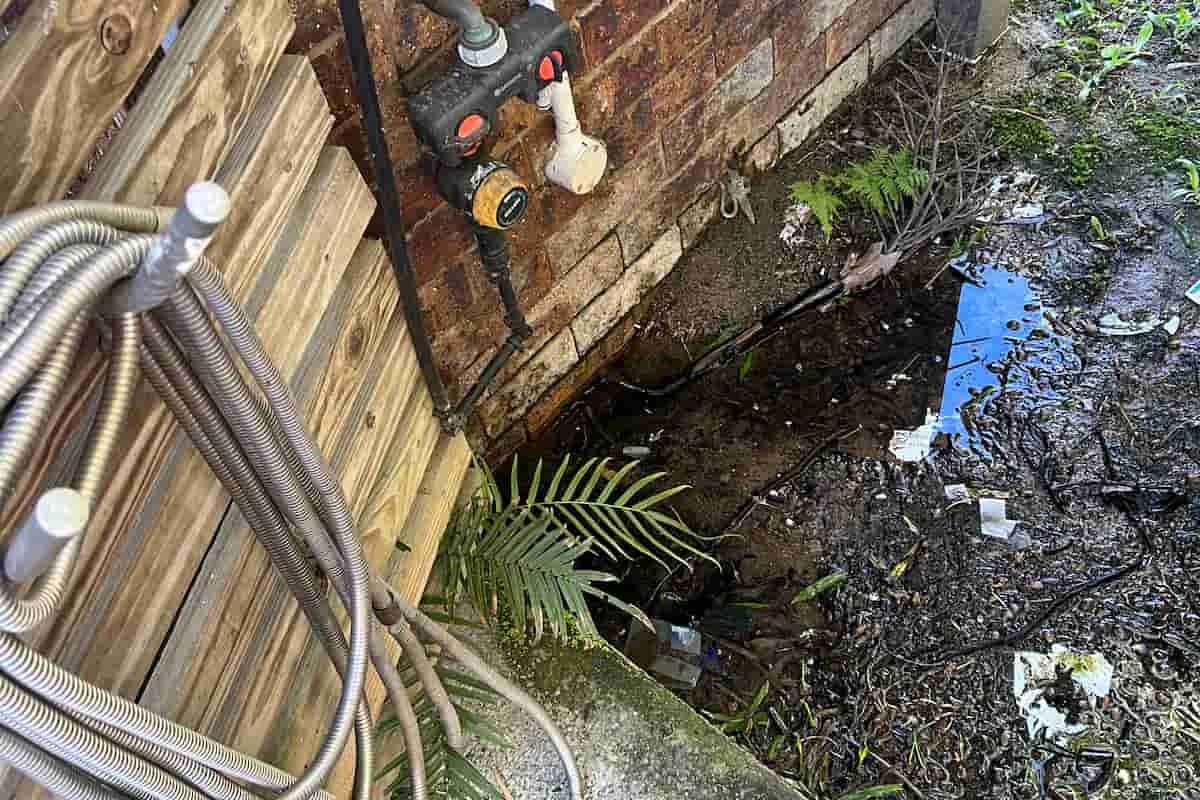 Outdoor tap leak causing pooling water near house wall and garden hose setup.