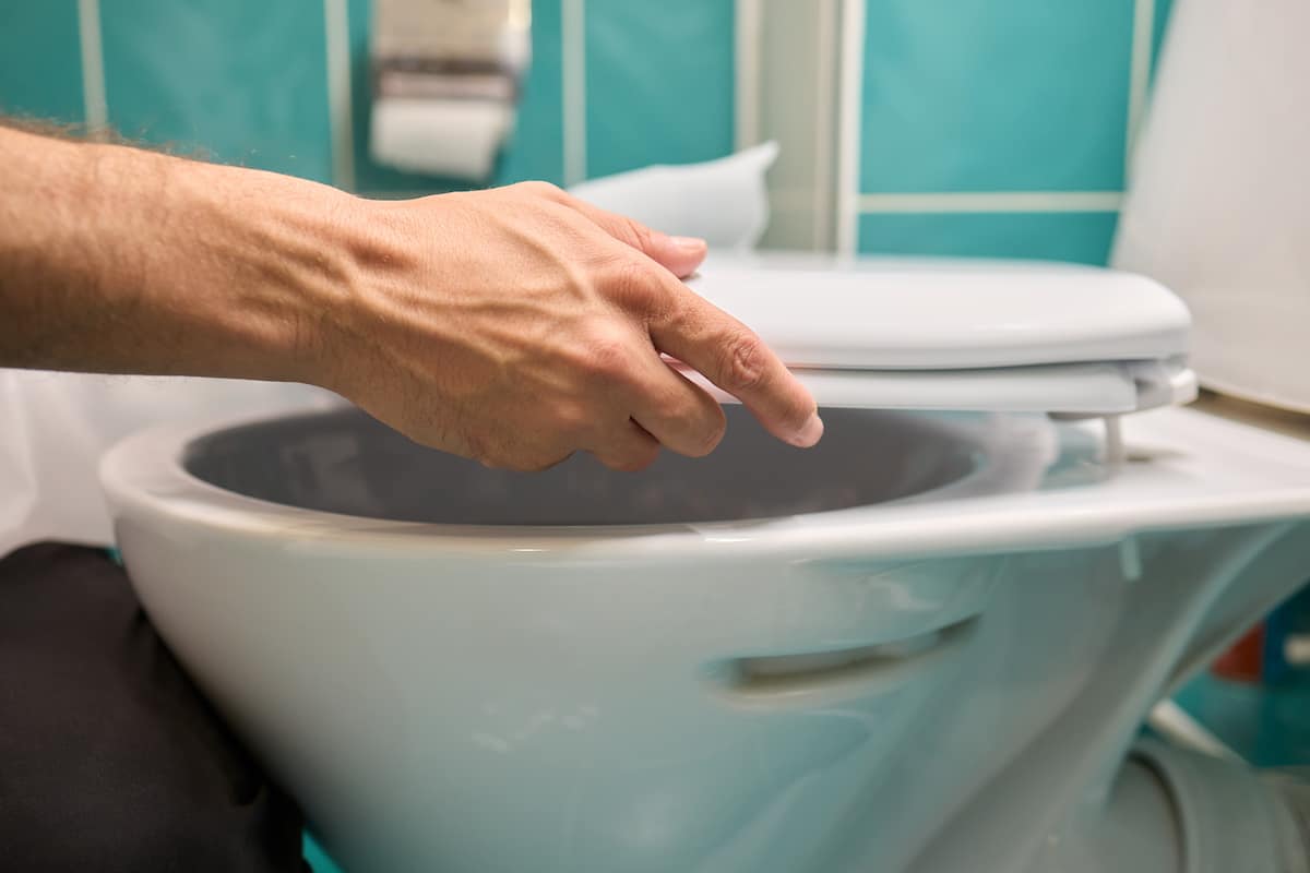 Plumber replacing a toilet seat during a toilet replacement job in a residential bathroom.